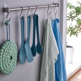 Three blue kitchen utensils hang on hooks: spatula, spoon, and tongs. Next to them, striped and blue towels hang.