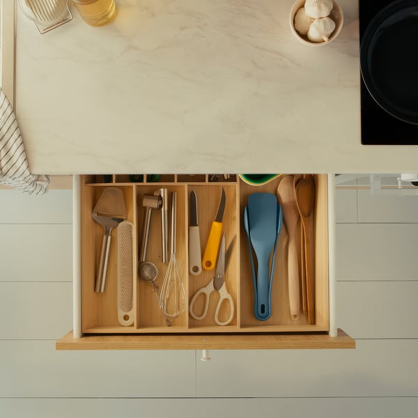 Organized kitchen drawer with utensils: tongs, spatula, spoon, scissors, and other tools neatly sorted in compartments.