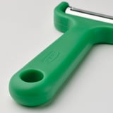 Green kitchen peeler with stainless steel blade, designed for long root vegetables. Secure handle with hanging hole.