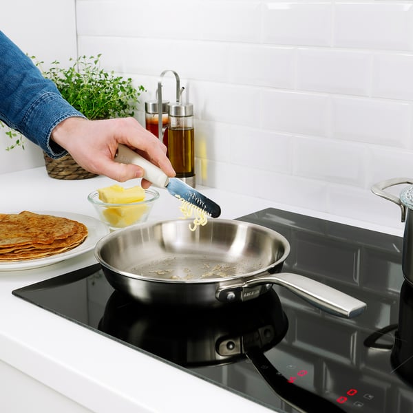 A person grates butter into a pan using a UPPFYLLD tool, demonstrating its versatile kitchen use.