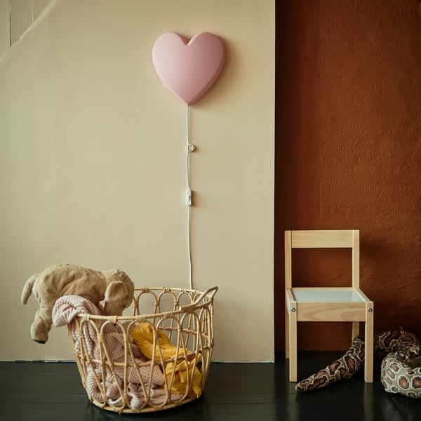 Heart-shaped lamp on wall, soft light, basket with blankets & teddy, small chair.