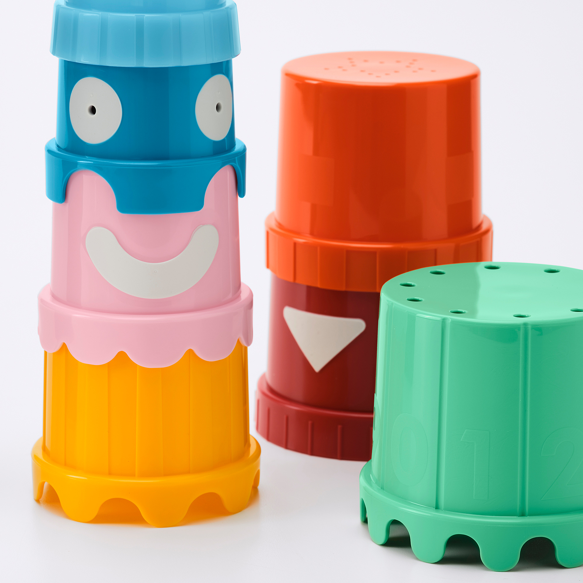 Four colorful plastic stacking cups with playful faces, brightly colored and arranged on a white surface.
