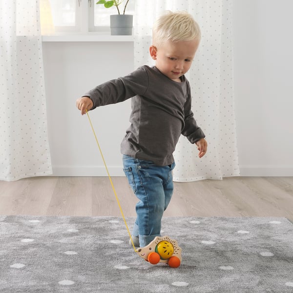 Blonde toddler pulls wooden hedgehog toy by string, promoting motor skills and learning.