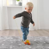 Blonde toddler pulls wooden hedgehog toy by string, promoting motor skills and learning.