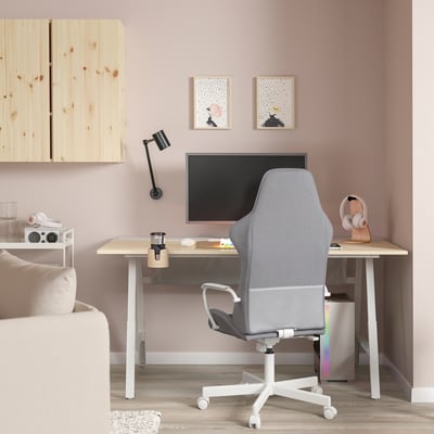 Home office setup with light grey UTESPELARE gaming chair, monitor, headphones, and shelves on light pink wall, partially visible sofa.