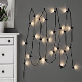 UTSUND string lights on gray wall, cozy, wavy, slim, floor to ceiling, with dresser and cactus picture.