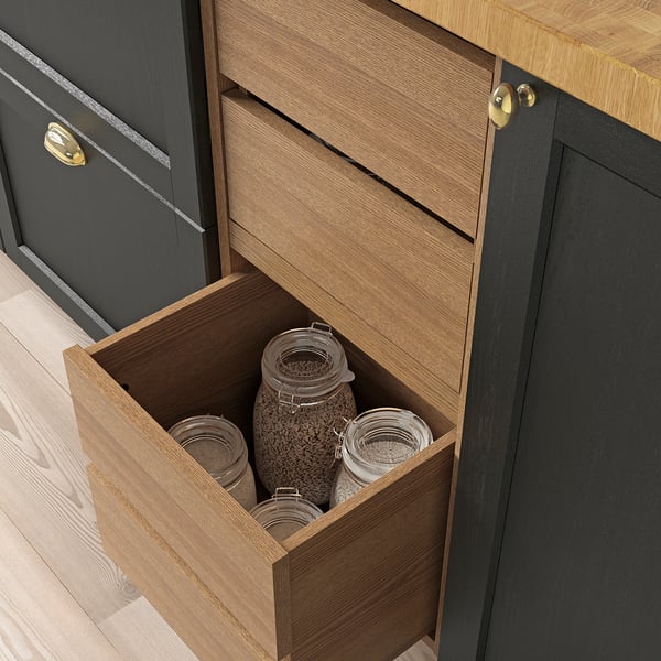 Wooden kitchen drawer with brass handle, partially open, revealing glass jars with contents visible.