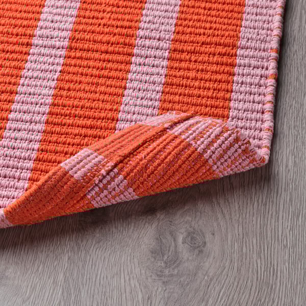 Bright striped door mat with orange and pink stripes folded on wooden floor.