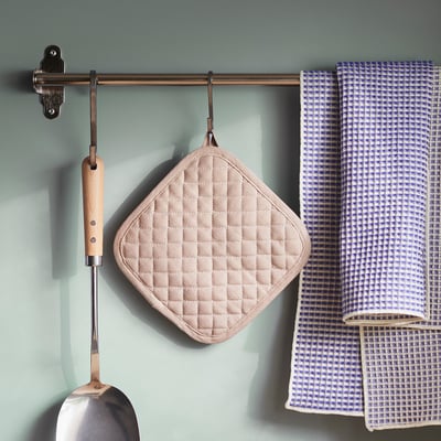 Modern kitchen storage with beige diamond vålvårdad potholder, checkered towel, and metal ladle.