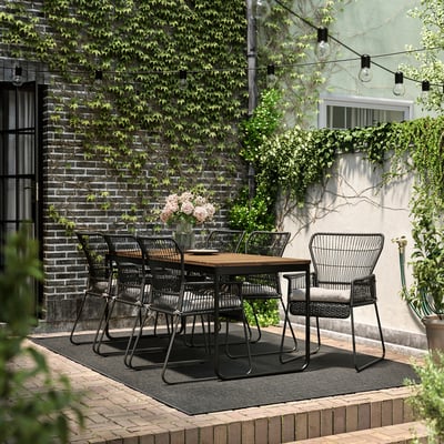 Cozy outdoor dining area with black wicker chairs and wooden table. Decorated with string lights and potted plants.