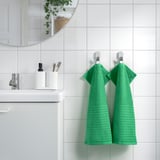Green VÅGSJÖN towels on hooks in modern bathroom, absorbent cotton.