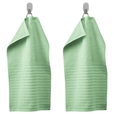Two green VÅGSJÖN towels hang neatly on silver hooks, showcasing a soft, textured ribs design in pure cotton.