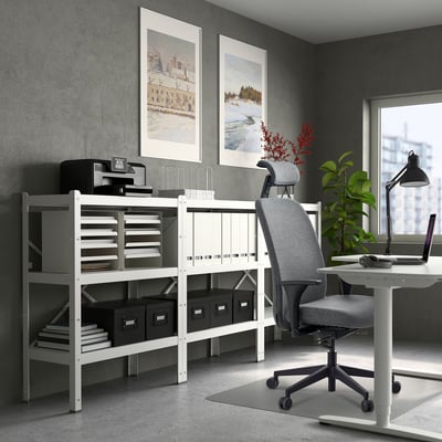 Modern home office with white desk, grey ergonomic chair, shelves, & laptop.