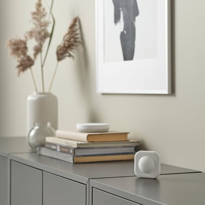 Small white VALLHORN motion sensor on shelf with books and vase.