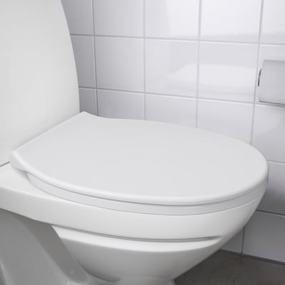Closed white toilet seat with rounded edges against tiled wall.