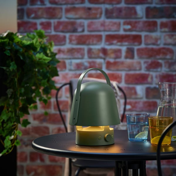 Green VAPPEBY speaker lamp on table with glasses and plant, playing music and lighting up.