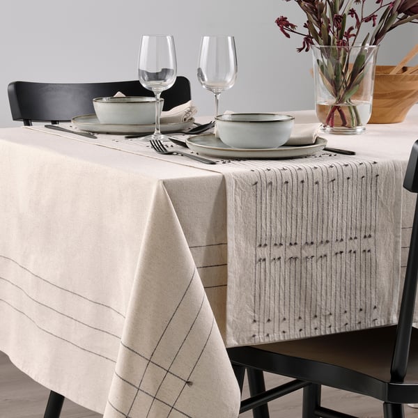 Table set with beige VÅRARV runner, plates, bowls, glasses, cutlery, chairs.