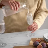Person pouring water from clear glass carafe into a wine glass, showcasing VARDAGEN glasswares versatility for serving beverages.