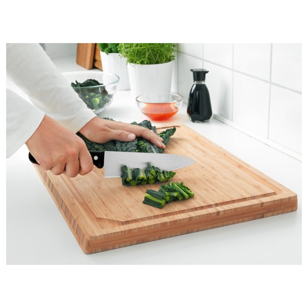 Person cutting vegetables on a wooden cutting board with a sharp stainless steel knife.