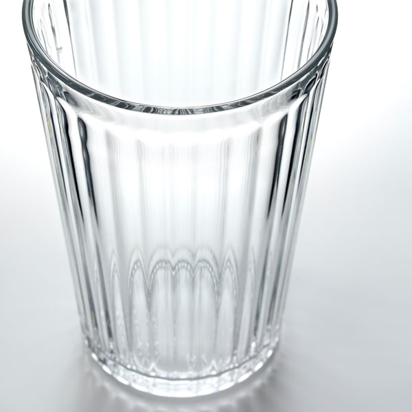 Glass cup with vertical ridges, clear and transparent, resting on a white surface.