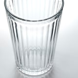 Glass cup with vertical ridges, clear and transparent, resting on a white surface.