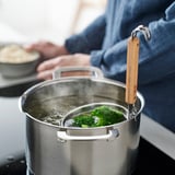 Boiling broccoli with wooden-handled strainer.