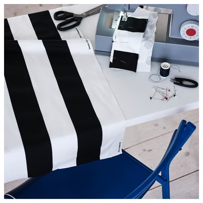 Black and white striped fabric on sewing table, scissors, thread, patterns, and blue chair nearby.
