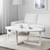 Modern living room with scandinavian-style coffee table. Coffee cup, remote, and magazines on shelves, near white sofa on light rug.