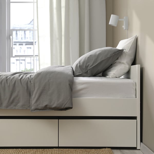 Modern bed frame with 2 rolled-out storage boxes under a neatly made gray comforter, showcasing practical space-saving design.