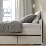 Modern bed frame with 2 rolled-out storage boxes under a neatly made gray comforter, showcasing practical space-saving design.
