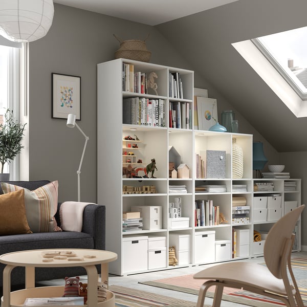 Modern home office with gray sofa, white bookshelves, wooden chair, and colorful rug.