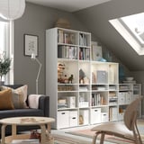 Modern home office with gray sofa, white bookshelves, wooden chair, and colorful rug.