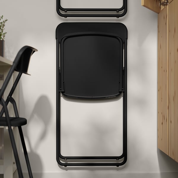 Folded black metal chair hung on wall, space-saving.