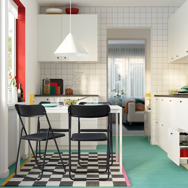Modern kitchen with VIHALS black metal chairs by small table. White pendant light above. Chequered rug under. Bright, colourful decor.