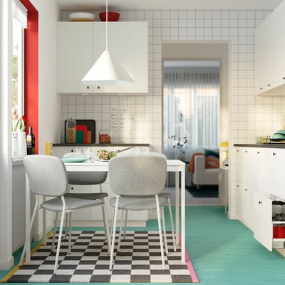 Modern kitchen with white VIHALS table, gray chairs, checkered rug, green floor, white cabinets, and hanging lamp.