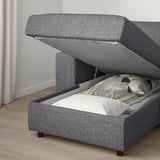 Modern upholstered sofa with open storage compartment, containing folded blankets and pillows.