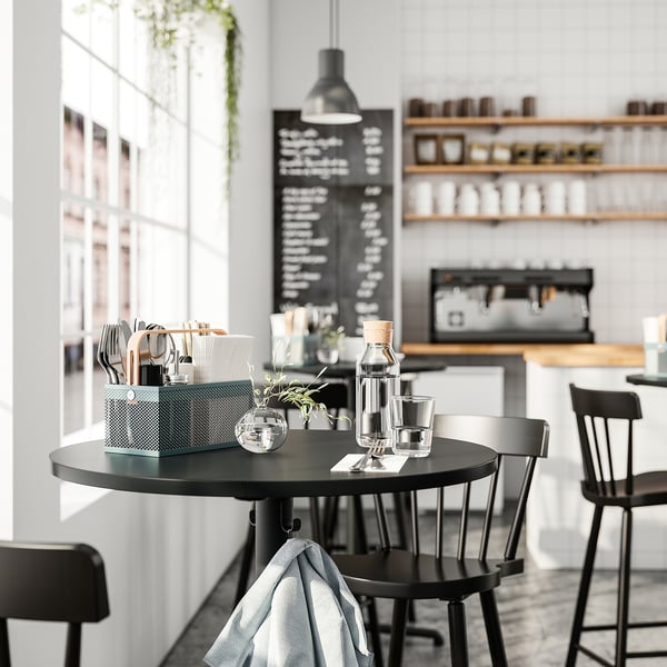 Black dining table with chairs, notepad, pen, glasses, VIMPELFISK cutlery, menu board, coffee station.