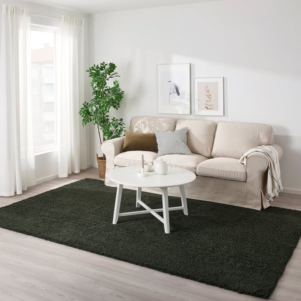 Dark green VINDEBÄK rug contrasts with light sofa and floor, centrally positioned for a cozy, lively feel in a bright living room.