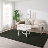 Dark green VINDEBÄK rug contrasts with light sofa and floor, centrally positioned for a cozy, lively feel in a bright living room.