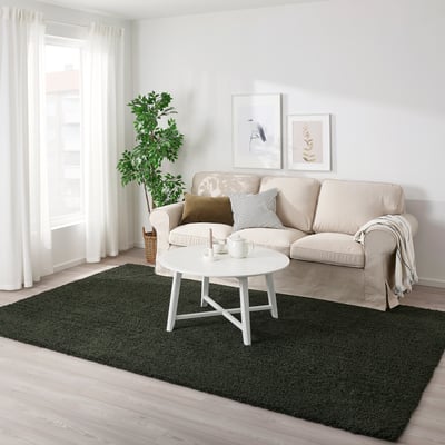 Dark green VINDEBÄK rug contrasts with light sofa and floor, centrally positioned for a cozy, lively feel in a bright living room.