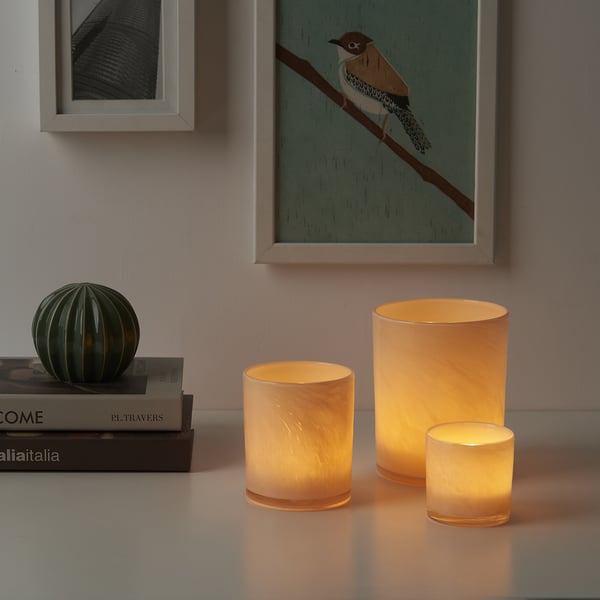Three glowing VINDSTILLA candle holders with unique patterns near books.