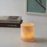 Illuminated glass candle holder on table, near books.