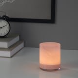 A lit candle in a pink glass holder sits on a table beside books and a clock, creating a cozy atmosphere.