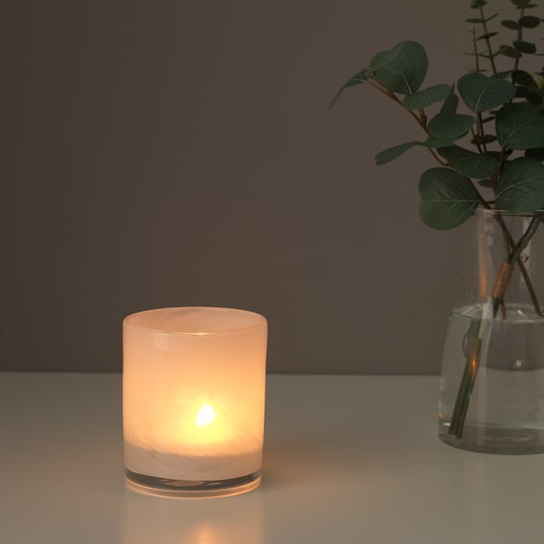 Lit candle & plants in vase on shiny surface.