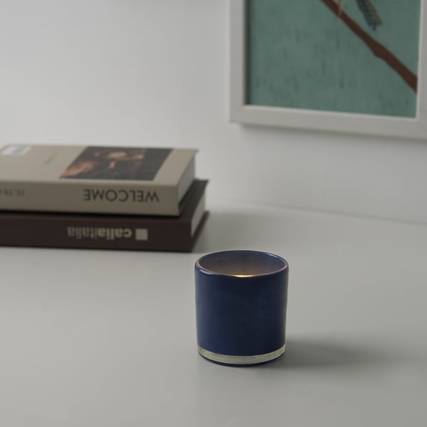 Dark blue candle holder on white table with books.