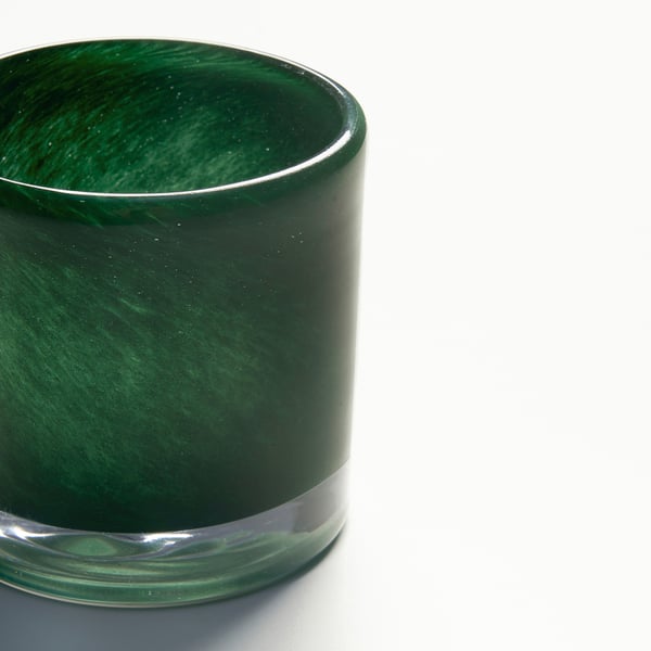 Close-up of a handmade green glass candle holder. Intricate swirl pattern reflects light, showcasing craftsmanship.