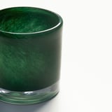 Close-up of a handmade green glass candle holder. Intricate swirl pattern reflects light, showcasing craftsmanship.