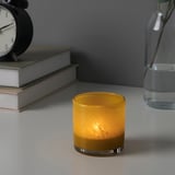 Yellow candle in glass holder on table with books and blue vase. Adds warmth.