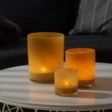 Three glowing amber glass candle holders of varying sizes on a round white table. The warm light brightens the cozy setting.