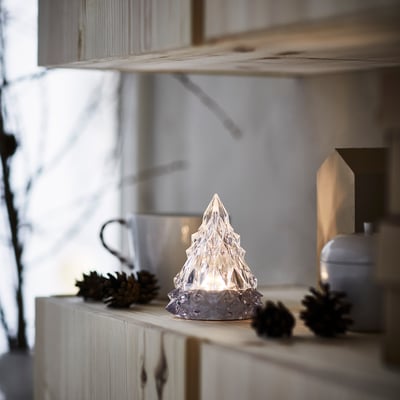 Small VINTERFINT tabletop light, clear, star-like shape, sits beside pinecones.